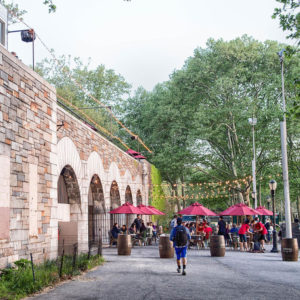 Riverside park venue, stone arches surrounded by greenery with red umbrellas set up at tables
